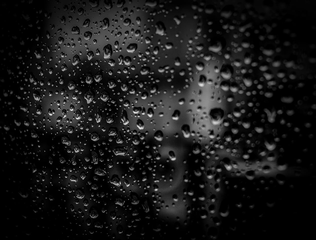 Close-up of raindrops on a glass surface with a dark background, creating an abstract and moody effect.